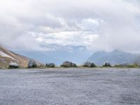 a black motorcycle parked in an empty area with mountains in the background, including snow and clouds