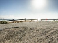 a red stop sign on a gravel road near the ocean with a bench on both sides