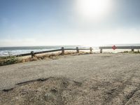 a red stop sign on a gravel road near the ocean with a bench on both sides