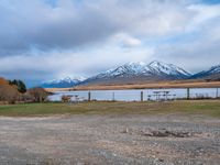 some picnic tables and a lake with snowy mountains in the back ground and clouds above