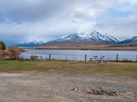 some picnic tables and a lake with snowy mountains in the back ground and clouds above