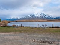 some picnic tables and a lake with snowy mountains in the back ground and clouds above