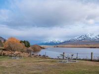 some picnic tables and a lake with snowy mountains in the back ground and clouds above