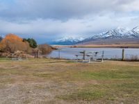 some picnic tables and a lake with snowy mountains in the back ground and clouds above