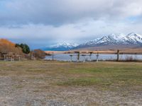 some picnic tables and a lake with snowy mountains in the back ground and clouds above