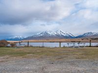 some picnic tables and a lake with snowy mountains in the back ground and clouds above