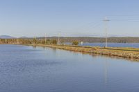 a train passes by a river in the distance surrounded by hills and trees, with power poles