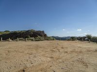 the view of a hill and lake from a dirt trail, near a fenced in area