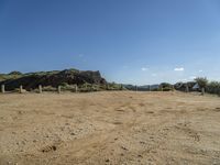 the view of a hill and lake from a dirt trail, near a fenced in area