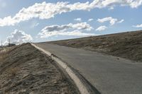 a dirt hill with an empty road and some building under the clouds and a bright sun