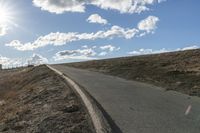 a dirt hill with an empty road and some building under the clouds and a bright sun