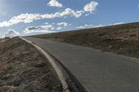 a dirt hill with an empty road and some building under the clouds and a bright sun