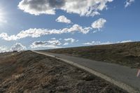 a dirt hill with an empty road and some building under the clouds and a bright sun