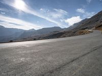 a man riding a motorcycle on the middle of a road surrounded by hills and snow capped mountains