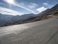 a man riding a motorcycle on the middle of a road surrounded by hills and snow capped mountains