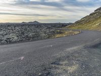 a motorcycle rider on an empty open road in front of the sun, and mountains