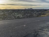 a motorcycle rider on an empty open road in front of the sun, and mountains