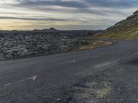 a motorcycle rider on an empty open road in front of the sun, and mountains