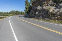 a motorcycle is on a paved highway with a lake in the background with a large cliff