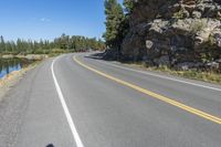 a motorcycle is on a paved highway with a lake in the background with a large cliff