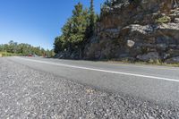 a motorcycle is on a paved highway with a lake in the background with a large cliff