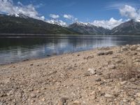 a lake with rocks on the shore and mountains in the background along side it and snow capped hills