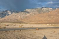 a man riding a bike on a paved road past mountains, clouds and a mountain range