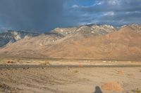 a man riding a bike on a paved road past mountains, clouds and a mountain range