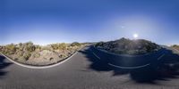 an 360 - view picture of the sun in the sky over a mountain road with curves of asphalt