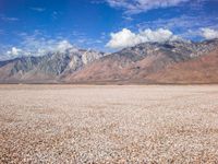 some mountains with rocks and gravel in between them as well as a large lake surrounded by grass and sand