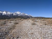 a lone person stands near rocky land with a mountain behind them, while a few snow capped peaks stand above