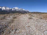 a lone person stands near rocky land with a mountain behind them, while a few snow capped peaks stand above