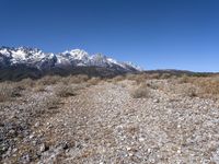 a lone person stands near rocky land with a mountain behind them, while a few snow capped peaks stand above