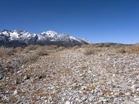 a lone person stands near rocky land with a mountain behind them, while a few snow capped peaks stand above