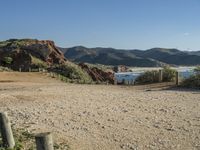 a dirt road surrounded by rocks, mountains and ocean with a wooden fence in the middle