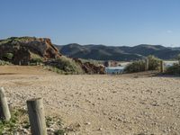 a dirt road surrounded by rocks, mountains and ocean with a wooden fence in the middle