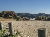 a dirt road surrounded by rocks, mountains and ocean with a wooden fence in the middle