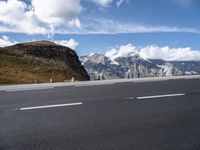 a large mountain with some snow on the top of it and an empty road with a few white lines on it