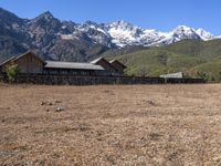 large mountain with snow covered peaks in the background and building near by field of dried grass