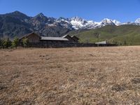 large mountain with snow covered peaks in the background and building near by field of dried grass