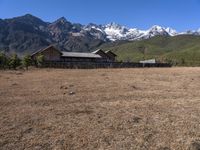 large mountain with snow covered peaks in the background and building near by field of dried grass