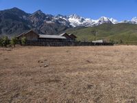 large mountain with snow covered peaks in the background and building near by field of dried grass