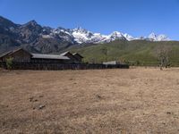 large mountain with snow covered peaks in the background and building near by field of dried grass