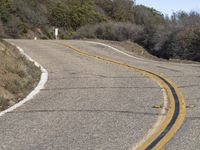 a mountain road leading up into the hills near trees and bushes on both sides of it