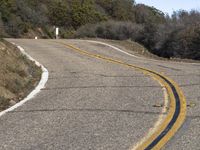 a mountain road leading up into the hills near trees and bushes on both sides of it