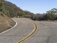 a mountain road leading up into the hills near trees and bushes on both sides of it