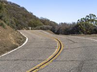 a mountain road leading up into the hills near trees and bushes on both sides of it