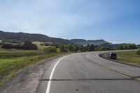 an empty road near mountains with hills in the background on a clear, sunny day