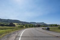 an empty road near mountains with hills in the background on a clear, sunny day