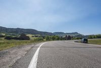an empty road near mountains with hills in the background on a clear, sunny day